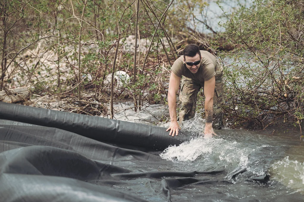 Worker positioning a large flood barrier tarp in water