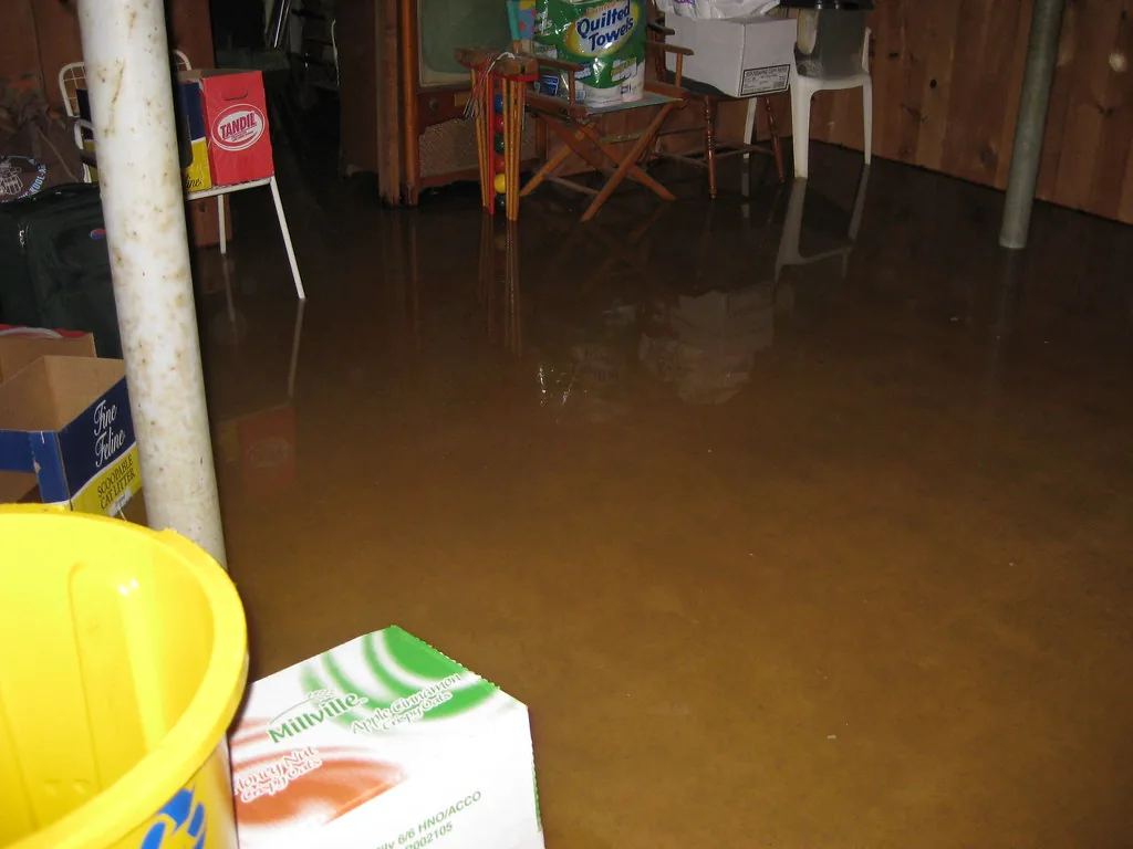 Flooded basement with brown standing water, yellow bucket and supplies visible